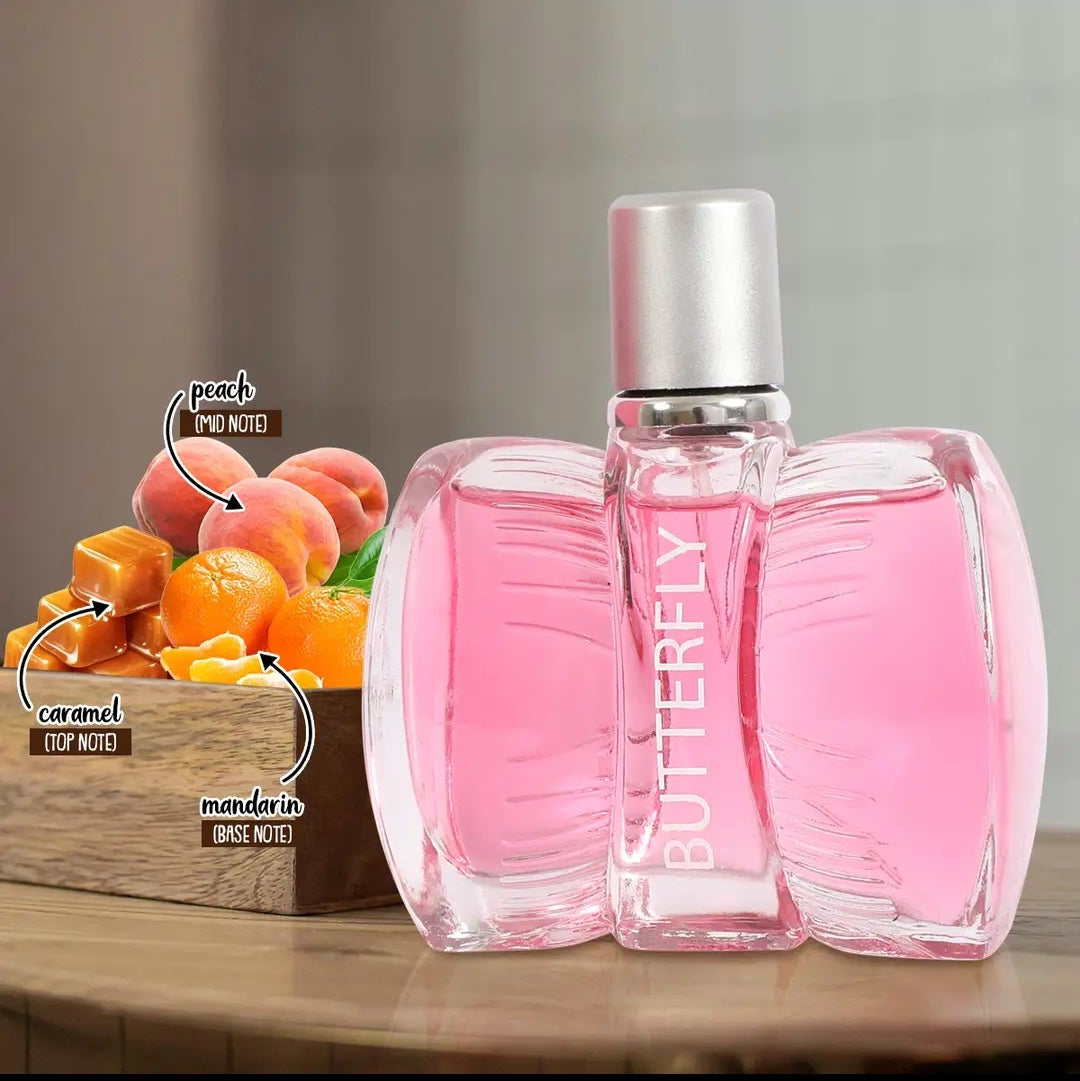 Pink perfume bottle labeled BUTTERFLY on a wooden surface, with a box of peach, caramel, and mandarin fruits in the background and scent note callouts.